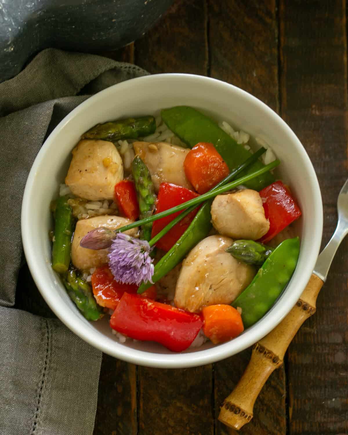 Chicken Stir Fry in a white bowl with chive garnish and a fork.