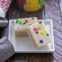 2 frosted sugar cookie bars topped with sprinkles on a square white plate.