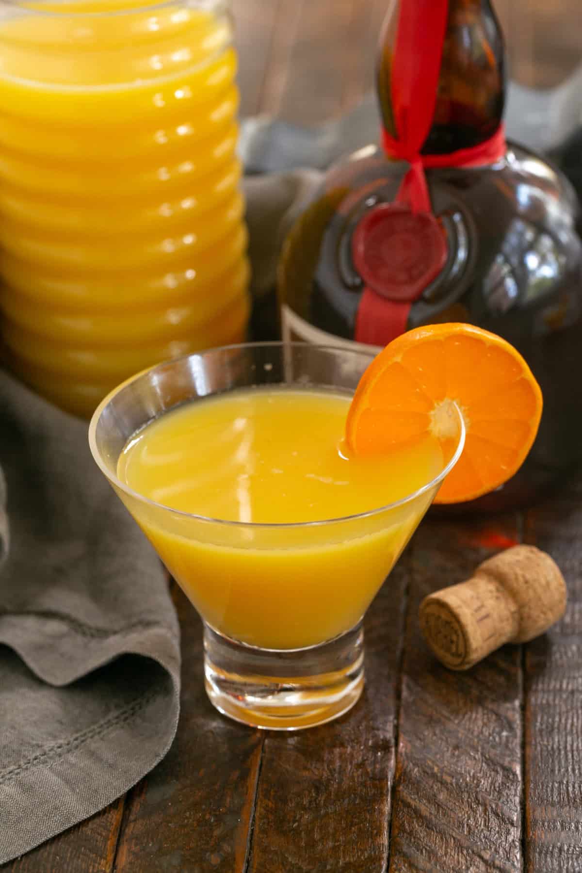 A grand mimosa cocktail in a glass with a clementine garnish on the rim.