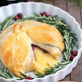 Cranberry Brie en Croute in a white ceramic dish garnished with rosemary and cranberries