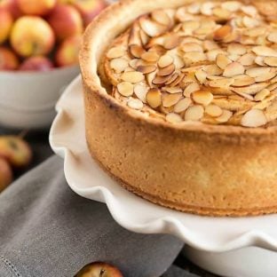 Cream Cheese Apple Torte on a ruffled white ceramic cake stand with lady apples to garnish