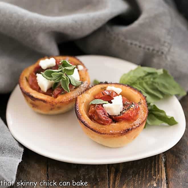 Cheese Straw Tomato Tartlets on an oval white plate with a sprig of basil.