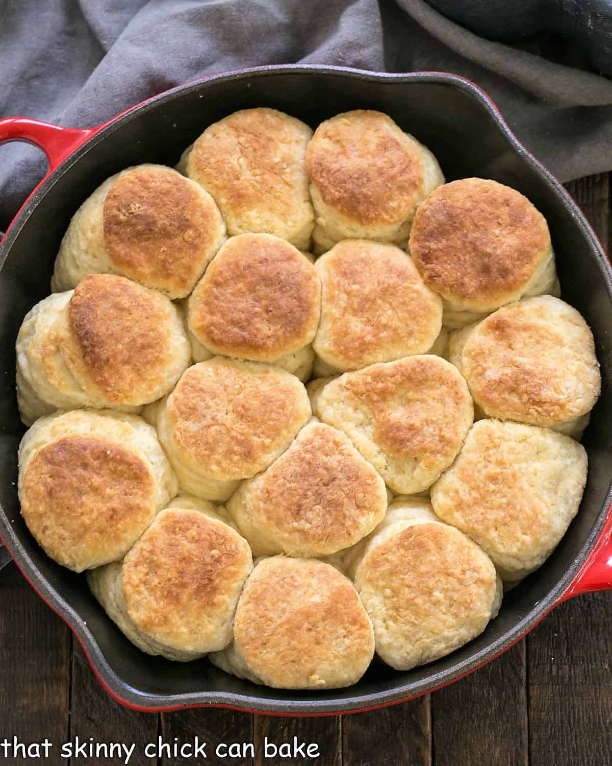 Overhead view of baked angel biscuits in a red cast iron skillet.