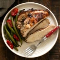 Overhead view of sliced chicken piccata on a white plate with a fork and green beans.