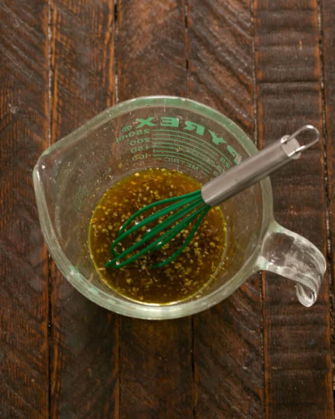 Italian vinaigrette in a Pyrex measuring cup with a small whisk.