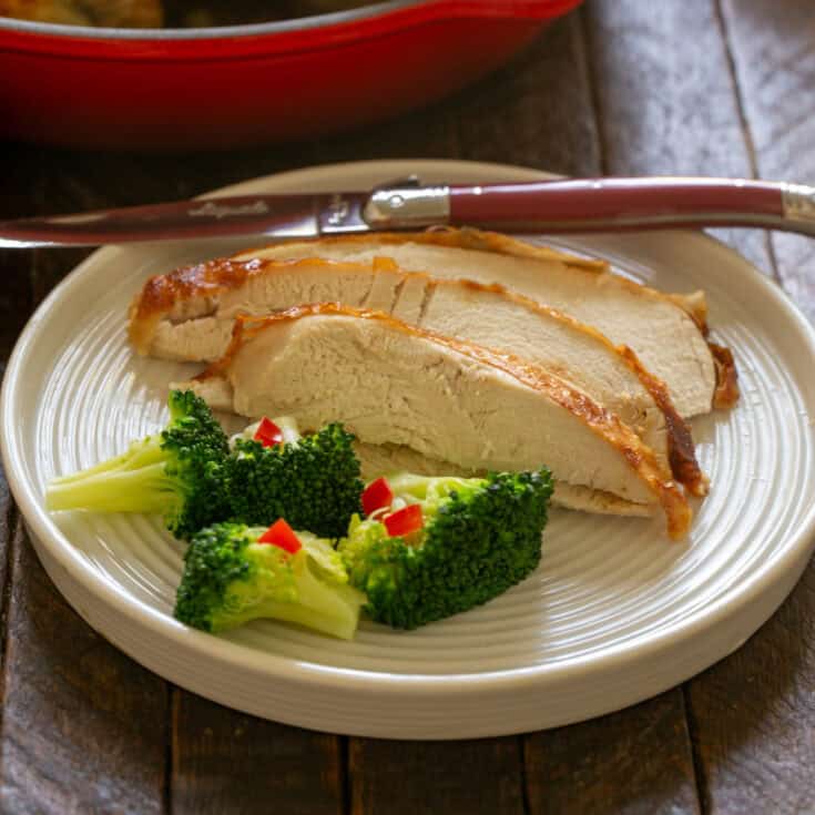 Slices of buttermilk brined chicken on a white plate with a knife and broccoli.