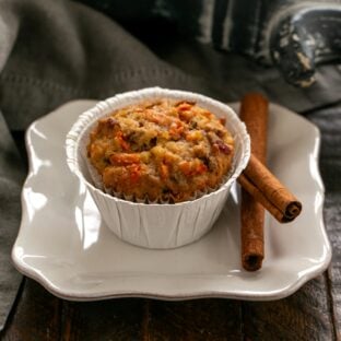 Morning glory muffin on a small white plate with cinnamon sticks.