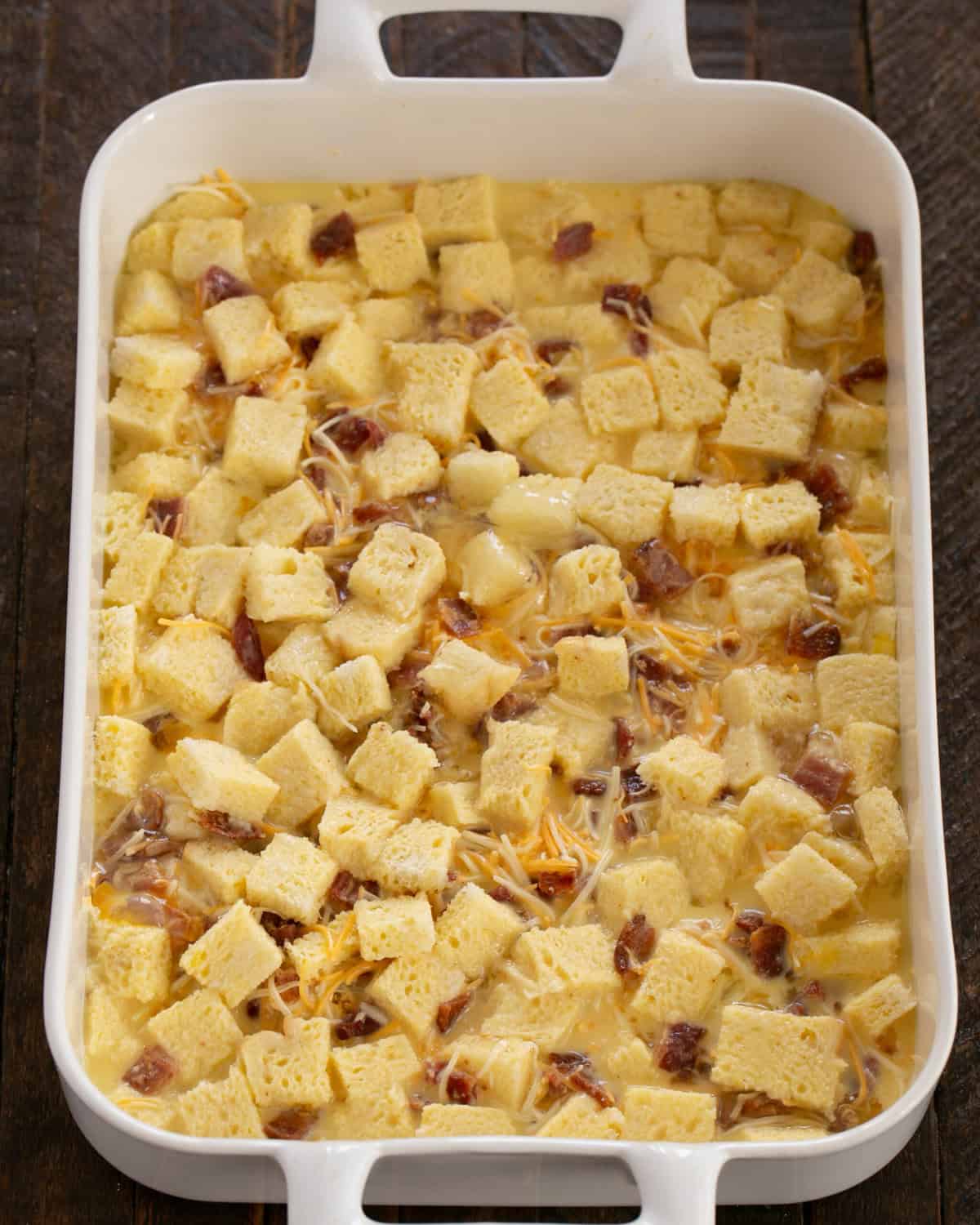 Cubed bread, baocn and cheese in a baking dish drizzled with butter.