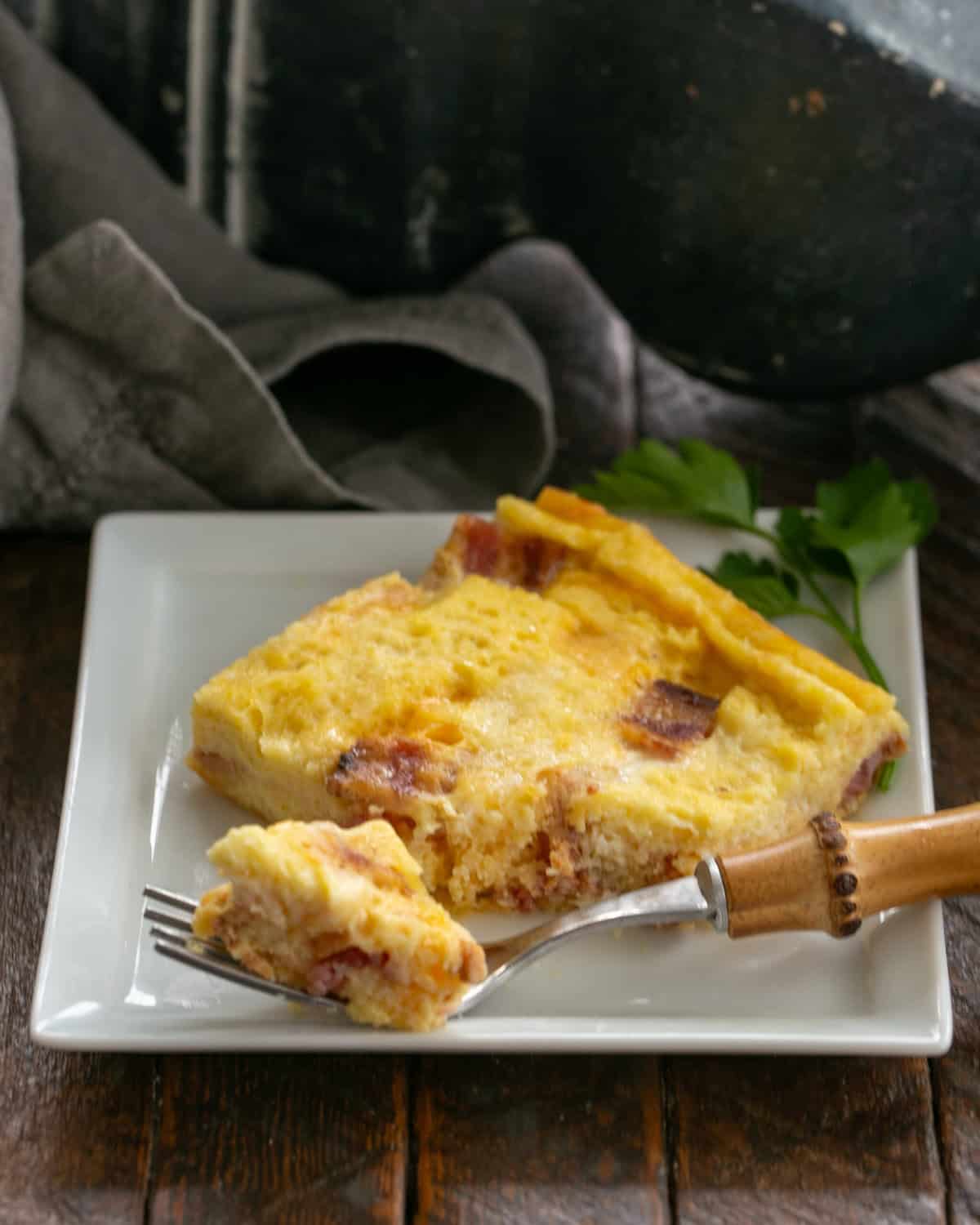 Slice of bacon and egg casserole on a white plate with a fork.