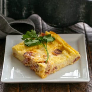 Slice of breakfast casserole on a white plate with a sprig of parsley.