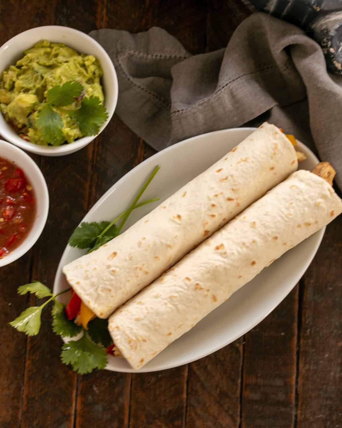 Overhead view of two chicken tortillas on a white plate with toppings to the side.