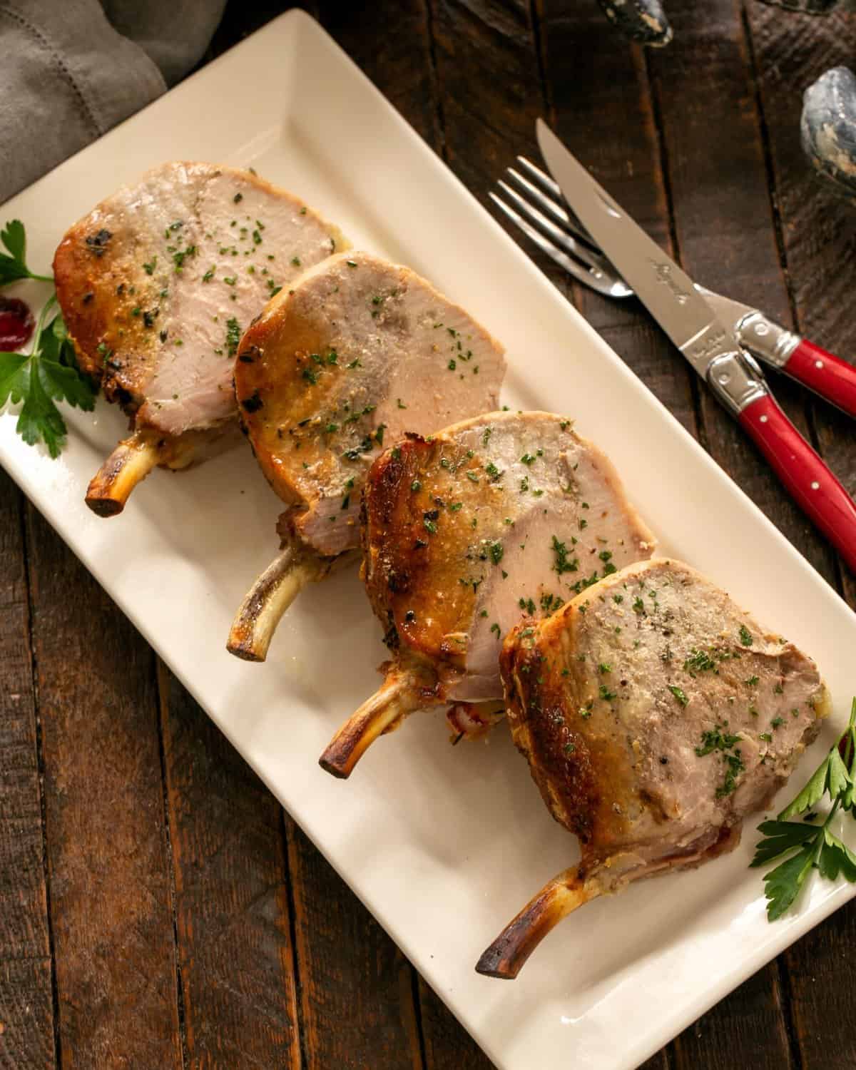 Sliced Crown Roast of Pork sprinkled with parsley on a white ceramic platter.